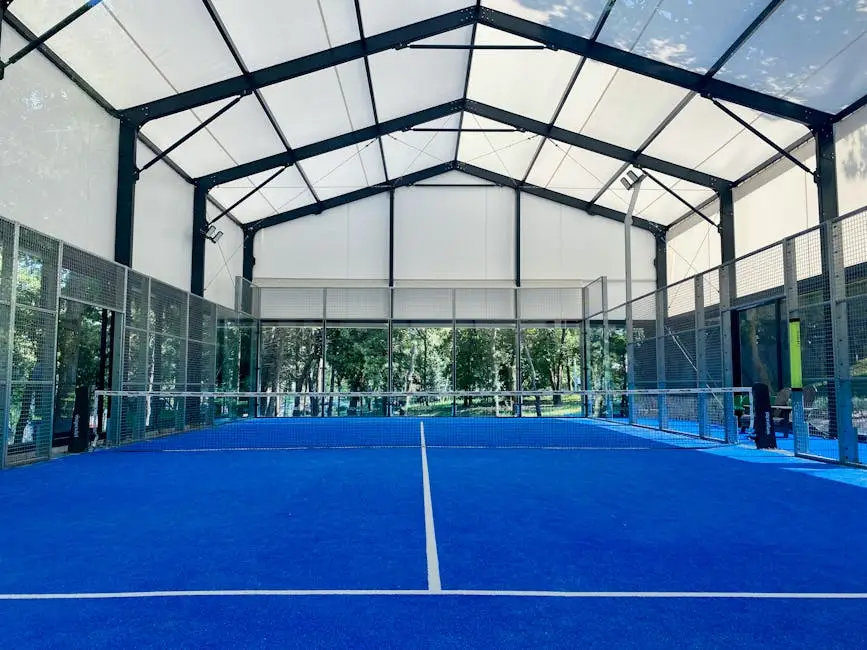 Spacious indoor padel court with vibrant blue flooring under a wide roof.